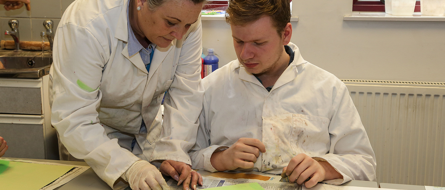 Learning Support Assistant leaning over helping male student with class work